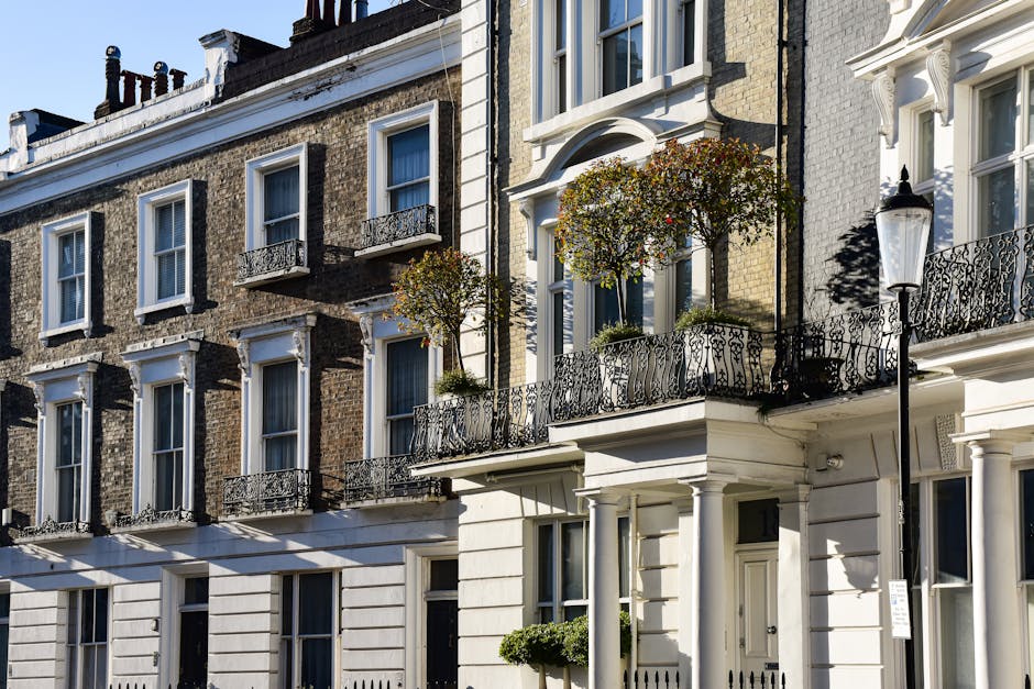 A row of Victorian-style terraced houses with bay windows and decorative mouldings, painted in varying pastel shades including light blue, beige, dark blue, and bright green. The buildings are constru